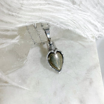 A silver heart-shaped pendant with a silver toned bezel wrapped around fools gold stone inside. The pendant is on a silver chain.